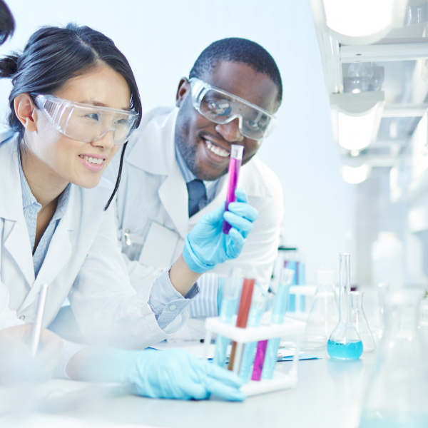 Two scientists in a lab, one holding a test tube, smiling and working together.